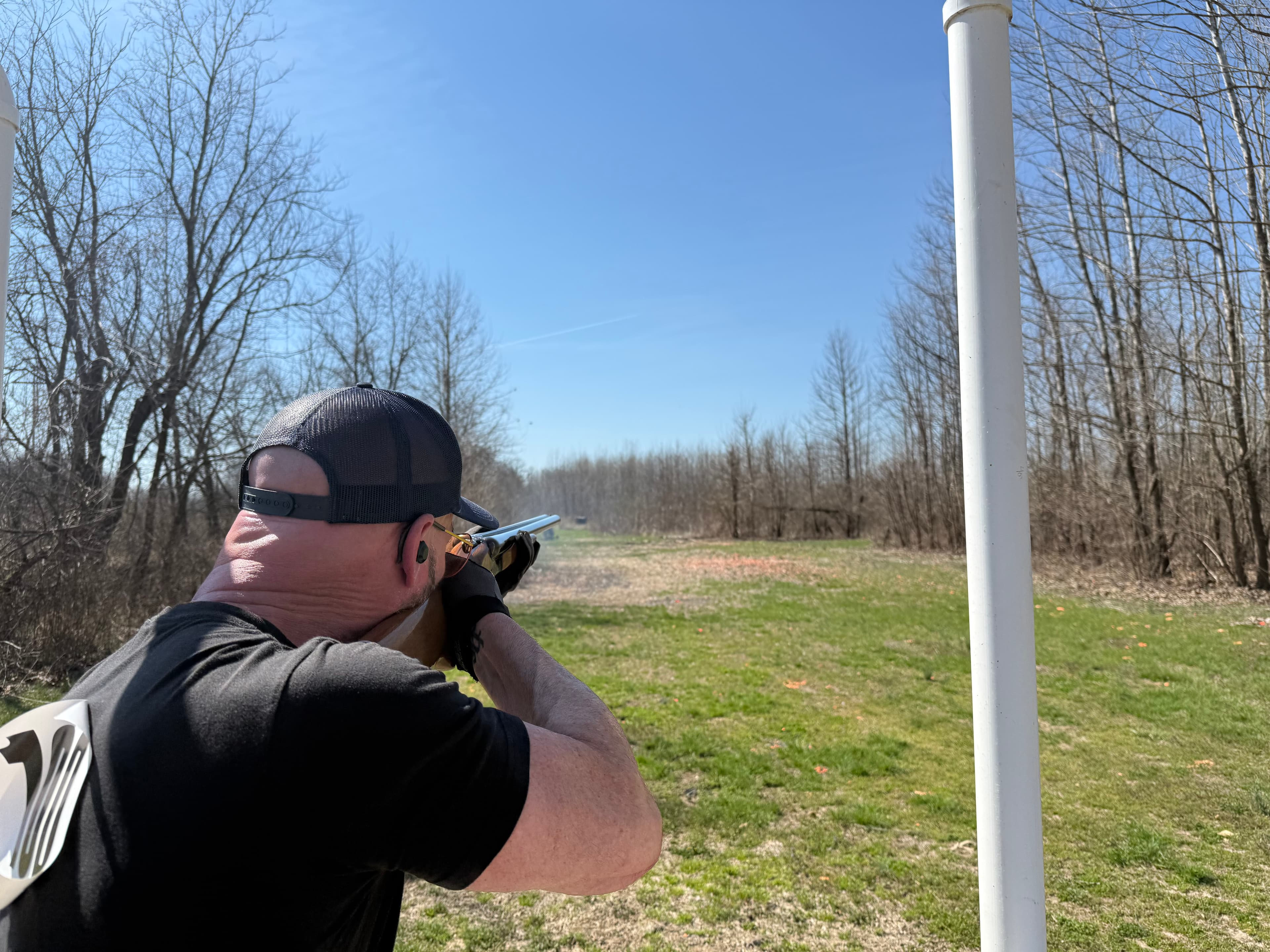 Jason aiming a shotgun at a sporting clays station on an open field.